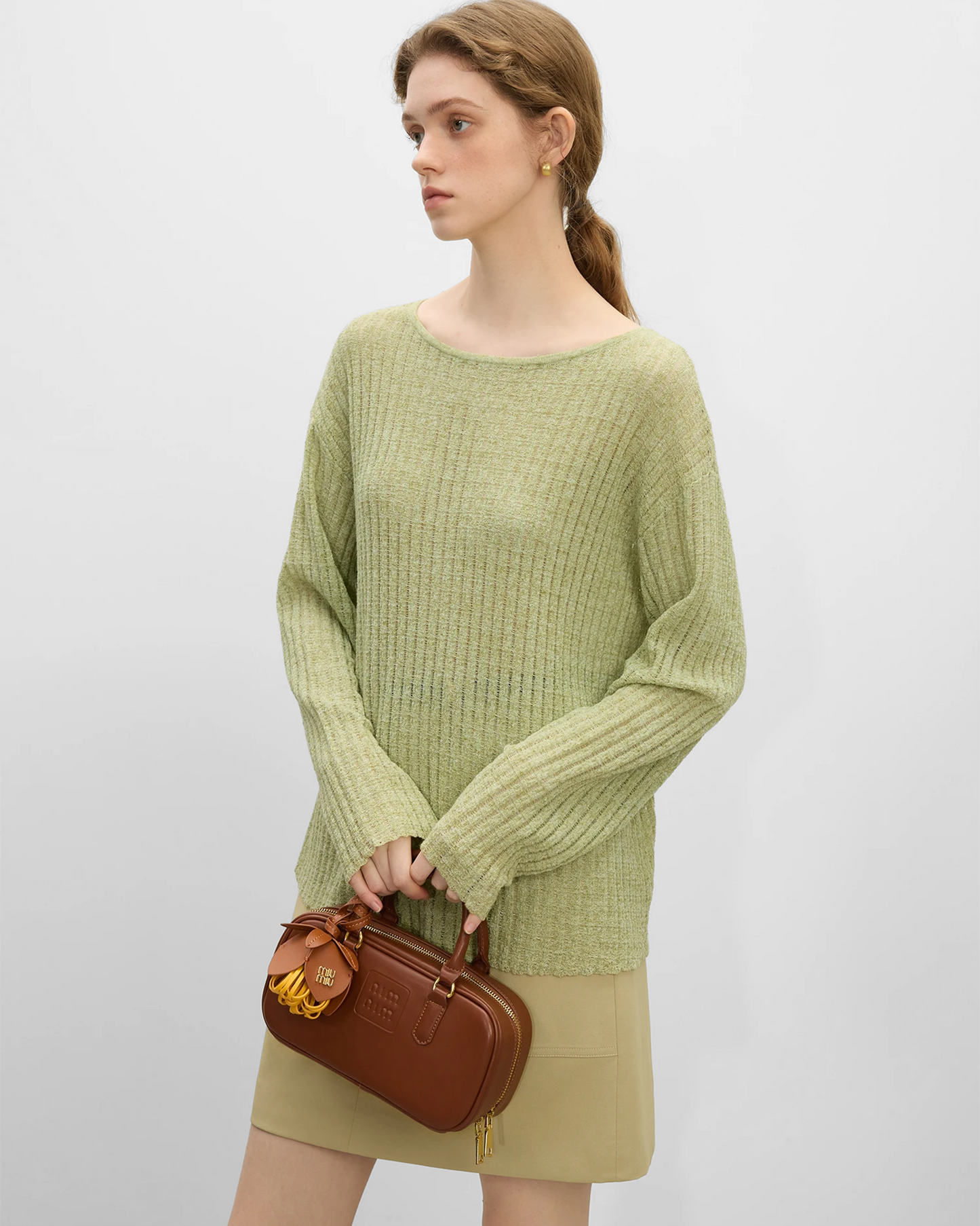 Mujer modelando un top de lino natural verde con mangas largas y una bolsa de mano marrón