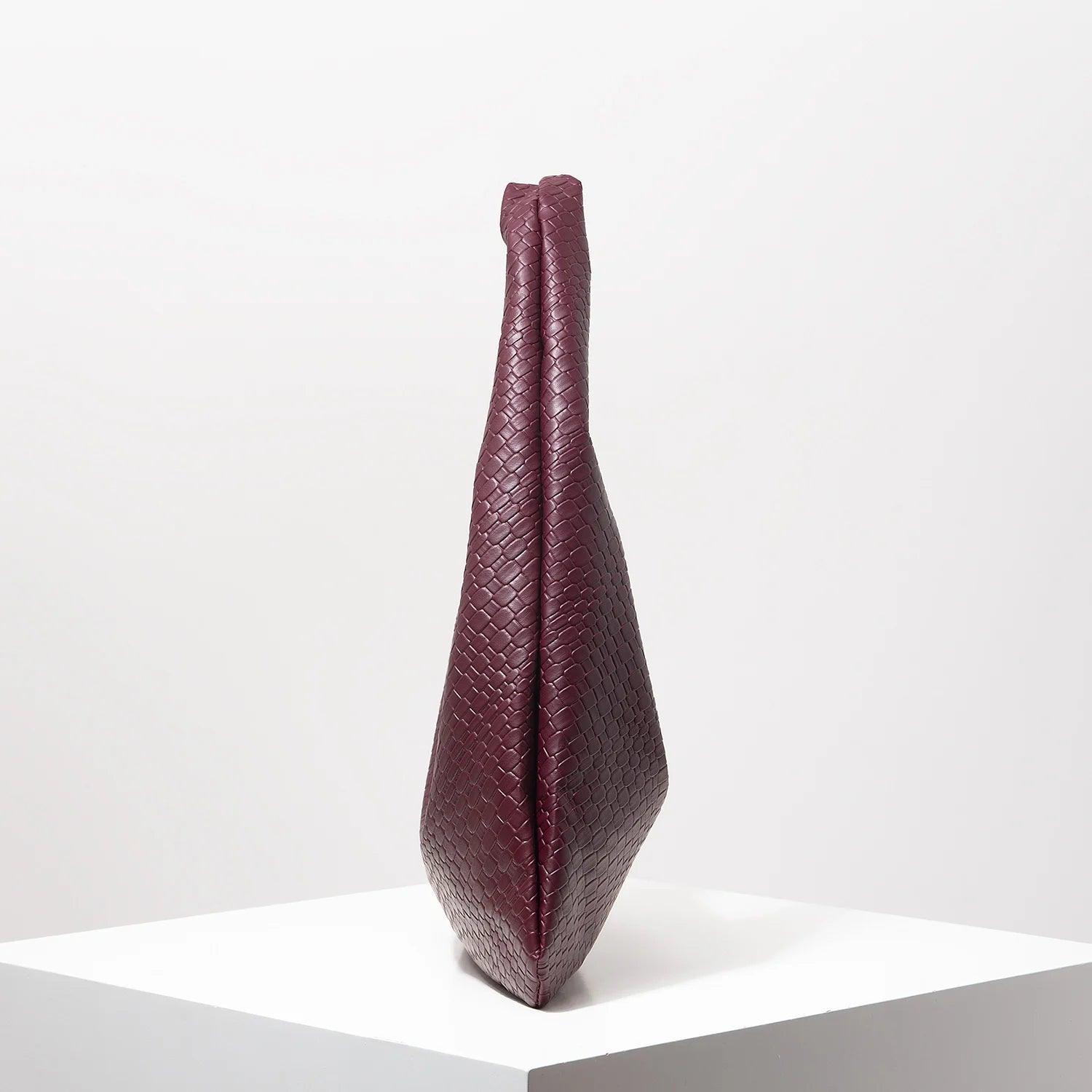 Bolso media luna trenzado en color burdeos, con diseño elegante y forma estilizada