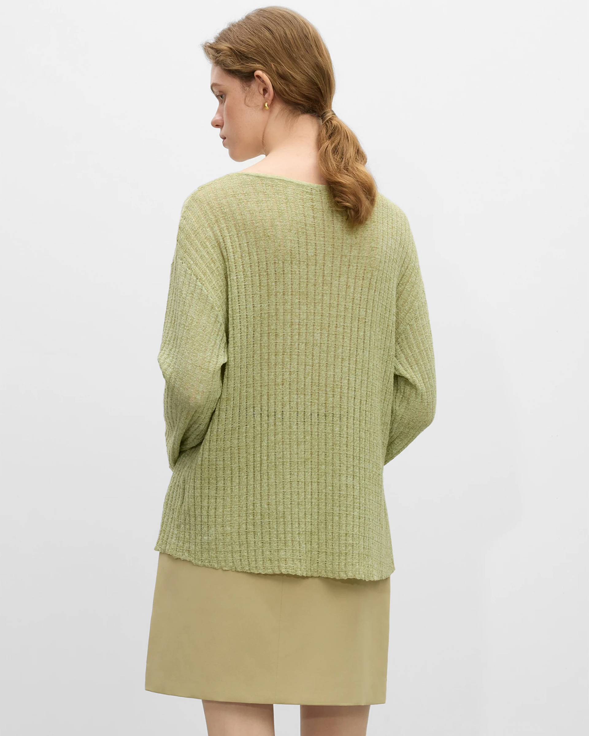 Mujer mirando hacia atrás con un top de lino natural verde claro y falda beige en un ambiente minimalista